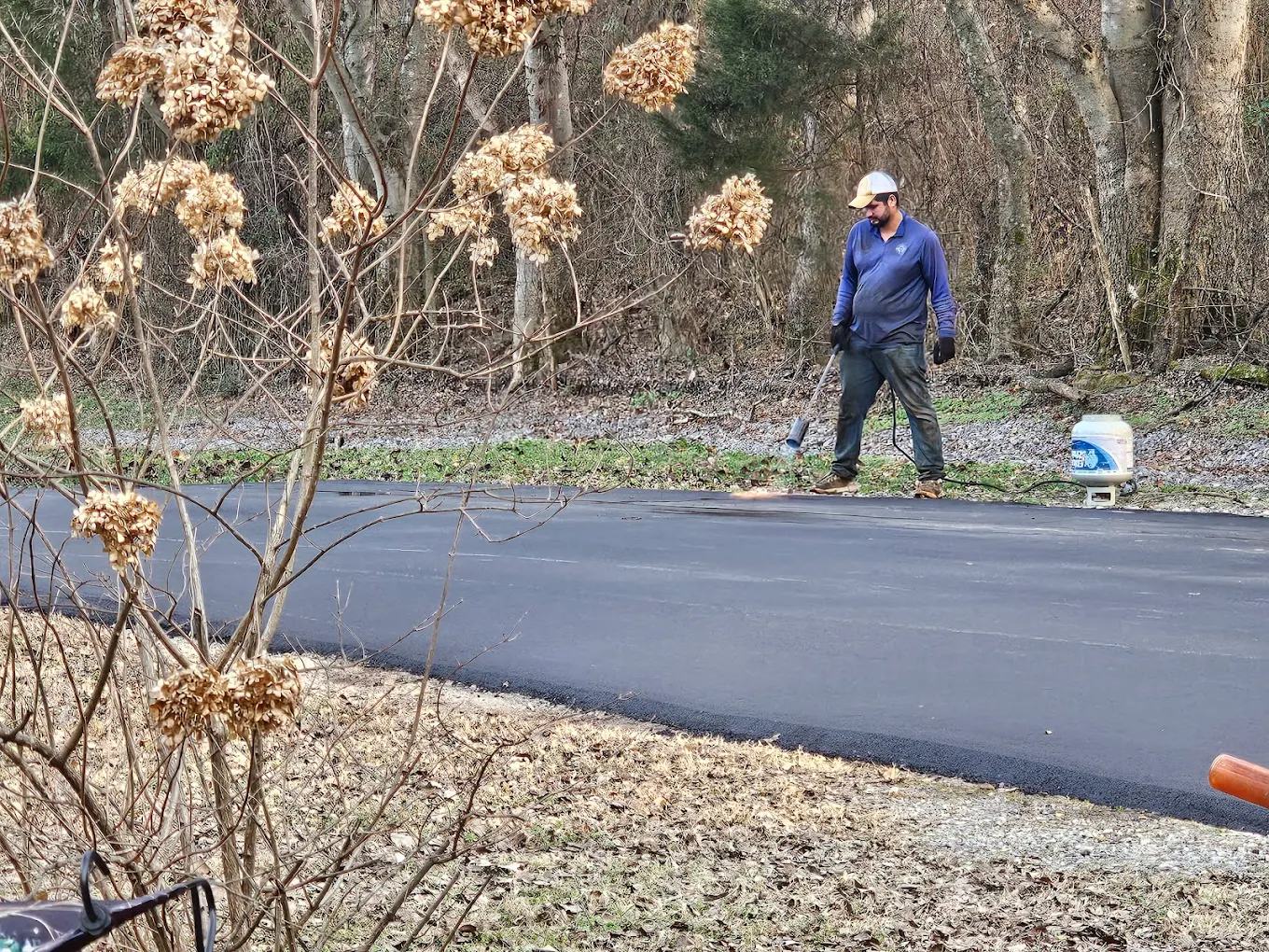 American Asphalt crew member applying fresh sealcoat to a residential driveway