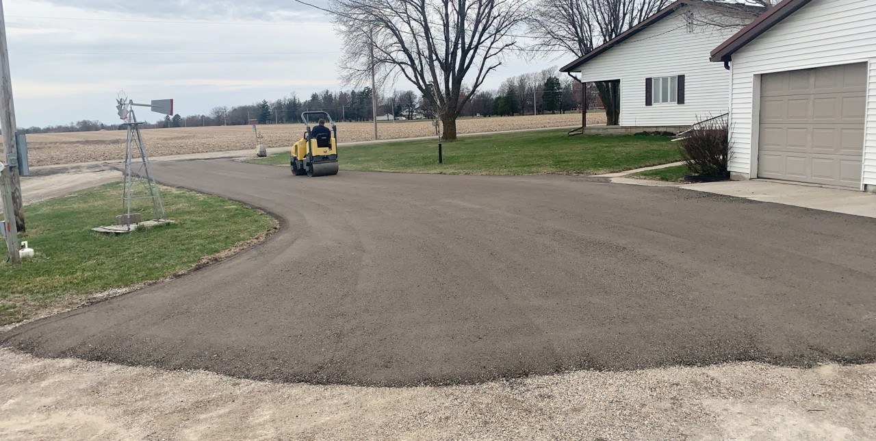 Recycled asphalt millings driveway being compacted with a roller at a rural home